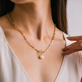 a gold chain link necklace with a pearl charm