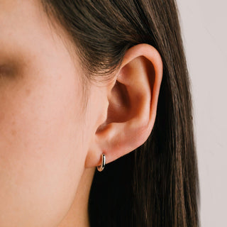 A close-up image of a person's ear wearing a gold-colored hoop earring.