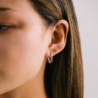Close-up of a woman's ear wearing a gold earring with a plain background