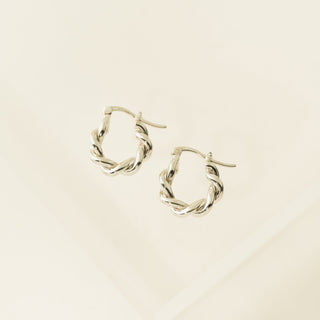 A close-up image of a woman's ear wearing a gold-plated hoop earring with a twisted texture.