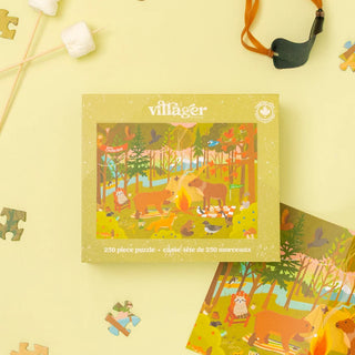 A Villager brand 250-piece jigsaw puzzle box featuring a whimsical forest scene with animals, shown on a pale yellow background with a few loose puzzle pieces and playful props around it.