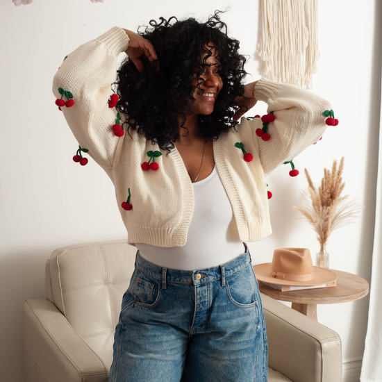 a women wearing a cardigan with embroidered 3d cherries on it.