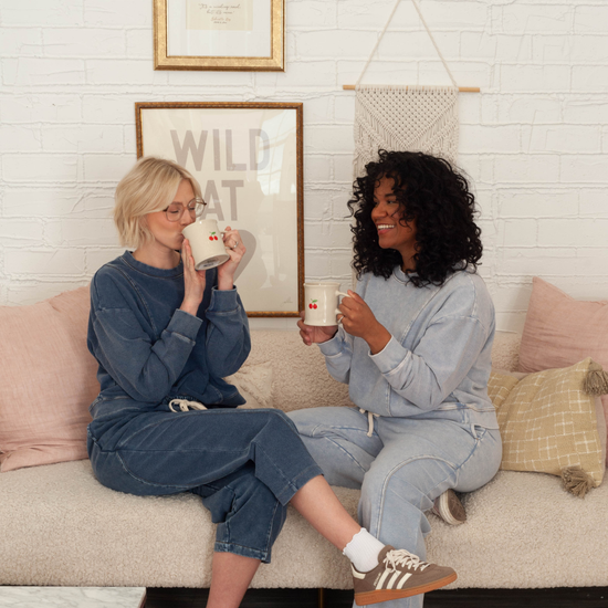 two women in cozy lounge sets drinking coffee on the couch