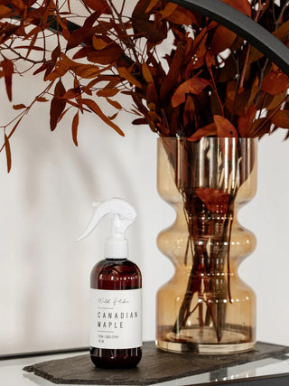 Bottle of 'Canadian Maple' with a vase and branches on a reflective surface