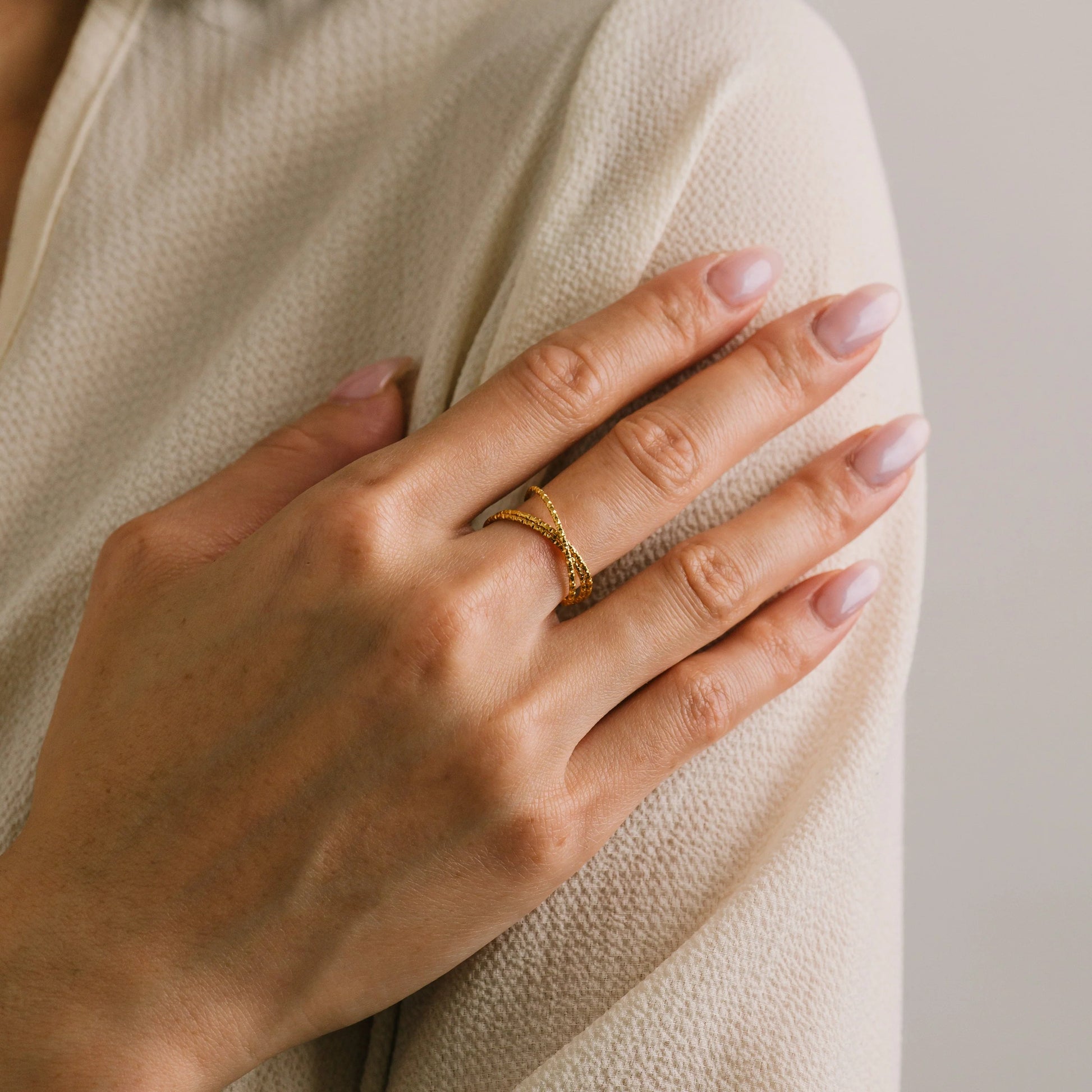 Hand wearing a gold ring on a neutral background