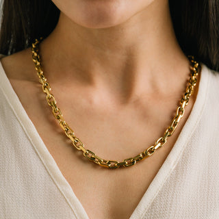 Gold chain necklace worn by a person against a neutral background