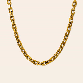 A close-up of a gold-toned chain necklace with large, polished oval links, arranged in a U-shape against a solid, warm off-white background.