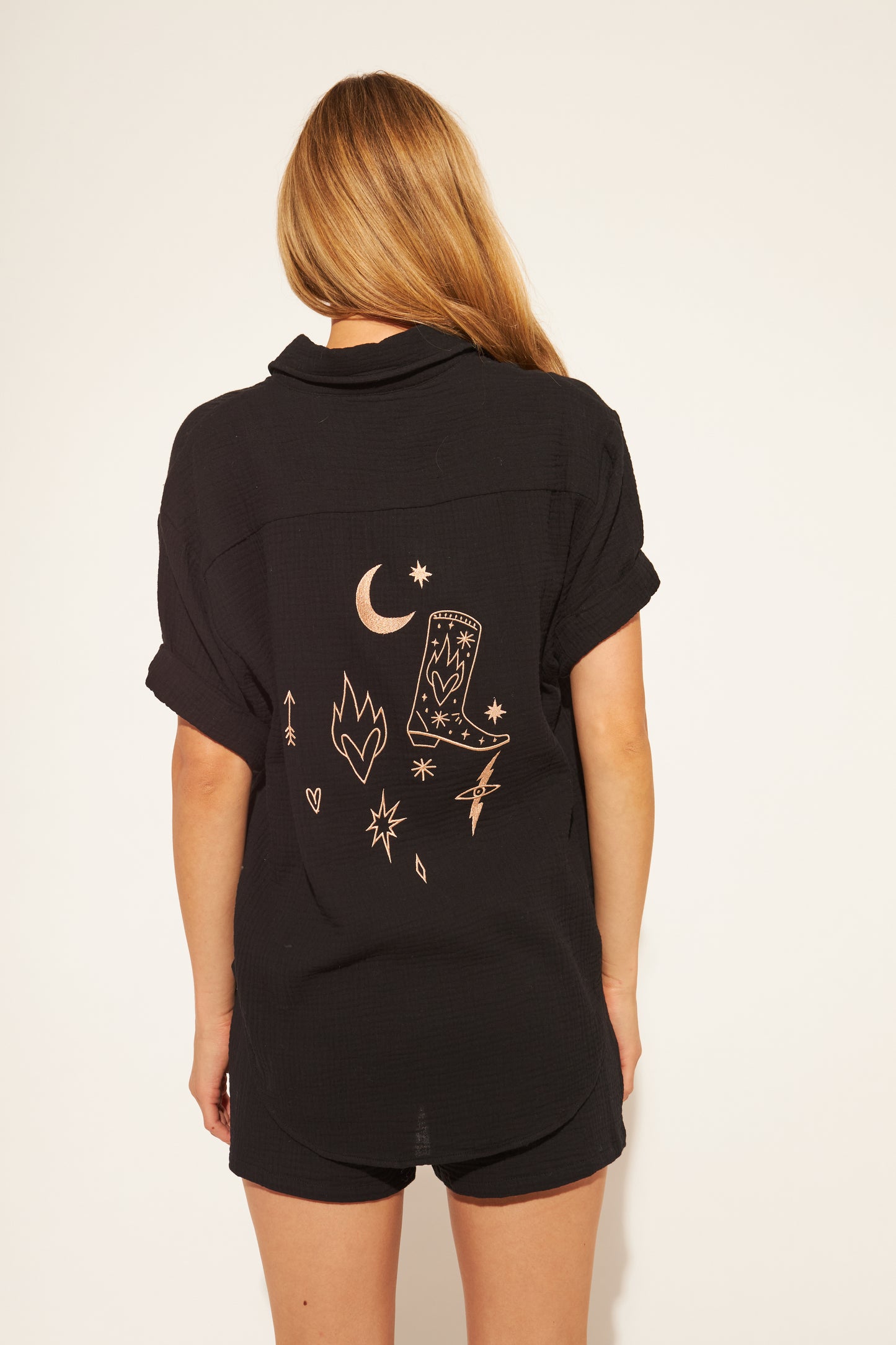 Person wearing a black shirt with embroidered designs on the back against a white background