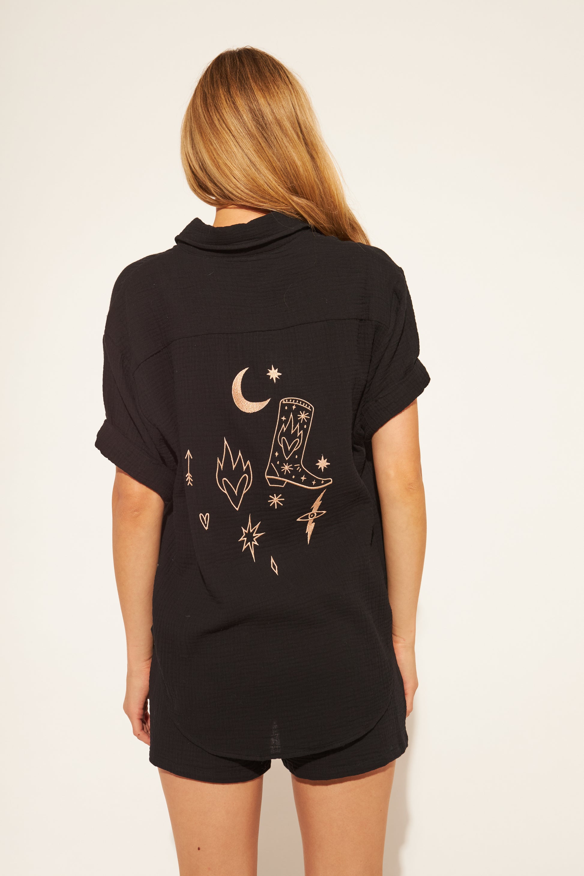 Person wearing a black shirt with embroidered designs on the back against a white background