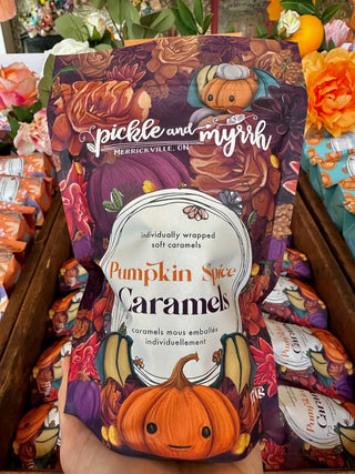 A hand holds a bag of Pumpkin Spice Caramels by pickle and myrrh. The packaging features a colorful autumn design with pumpkins, leaves, and flowers.