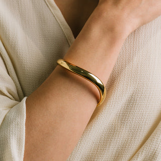 Gold bracelet on a wrist with a neutral background