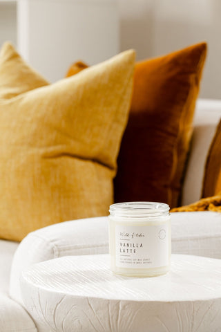Vanilla Latte candle on a white table with yellow and brown pillows in the background