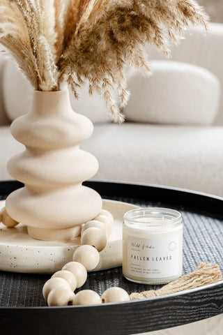 Decorative candle on a tray with a vase and pampas grass in the background