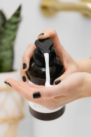 Hand using a black pump bottle to dispense liquid soap into another hand against a neutral background.
