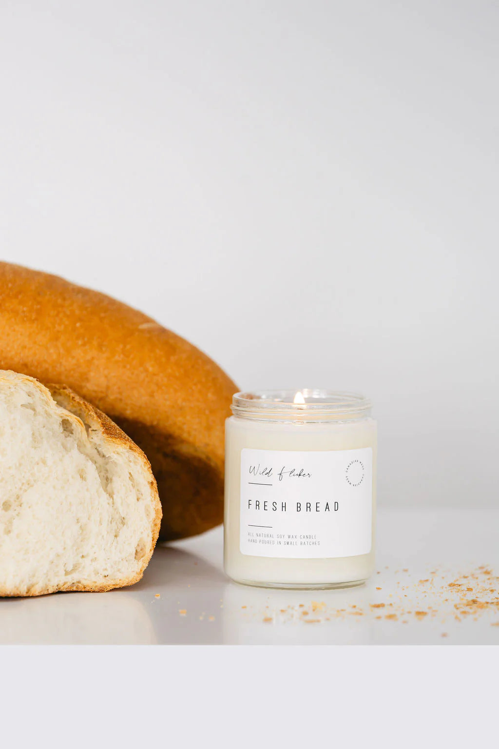 Candle labeled 'Fresh Bread' next to a loaf of bread on a white background