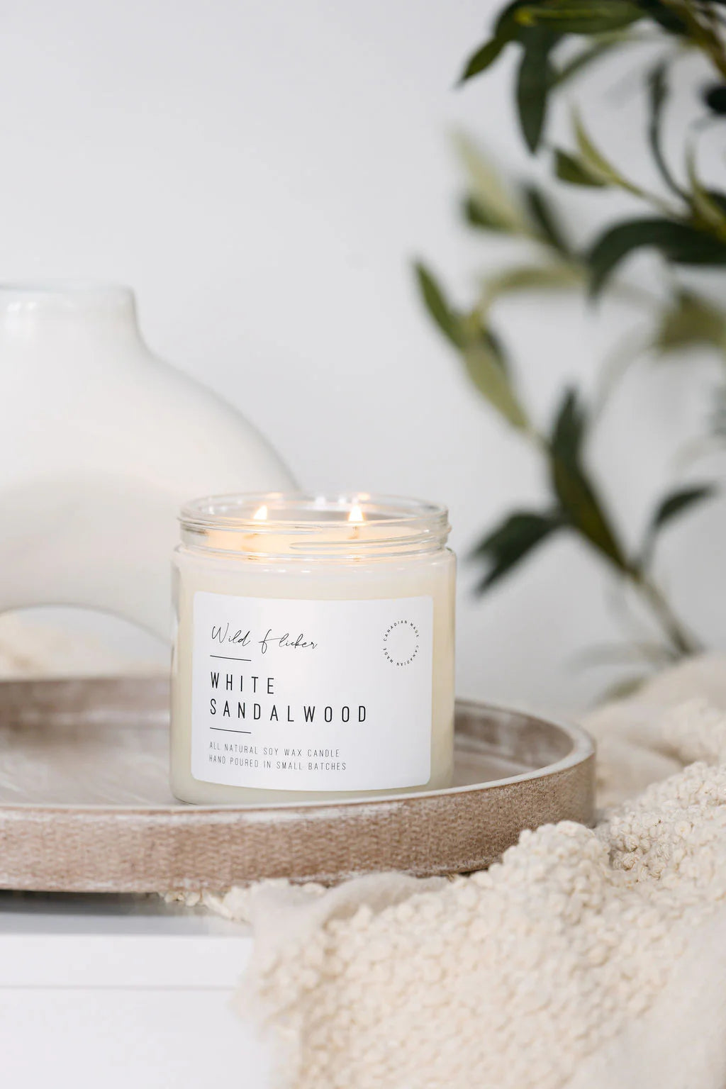 Candle labeled 'White Sandalwood' on a wooden tray with a blurred plant in the background