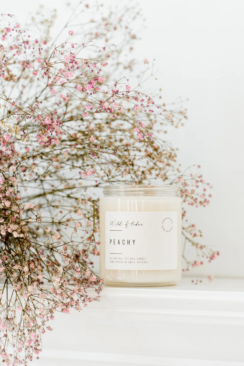 Candle labeled 'Peachy' with pink flowers in the background