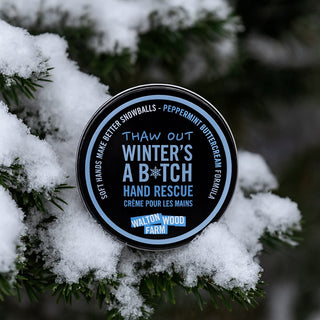 Hand cream container labeled 'Winter's A Bitch' on a snowy branch