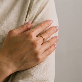 Hand wearing a gold ring on a neutral background
