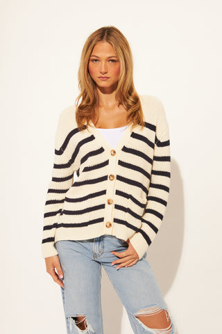 Woman wearing a striped cardigan and ripped jeans on a white background