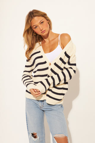 Woman wearing a striped cardigan, white top, and jeans on a plain background