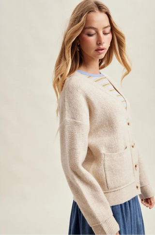 Woman wearing a beige cardigan over a blue shirt and skirt on a plain background