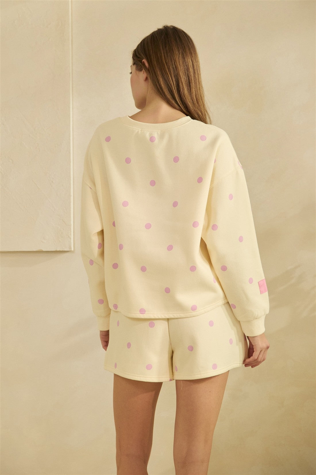 Person wearing a light yellow pajama set with pink polka dots on a beige background