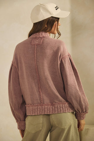Person wearing a pink knitted sweater and beige cap against a neutral background