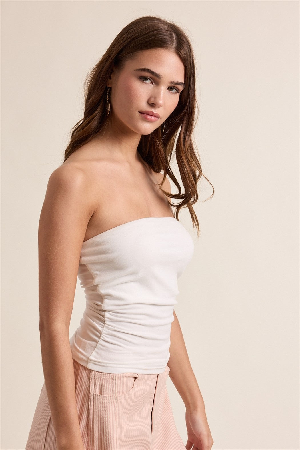 Woman wearing a white strapless top and pink pants against a beige background