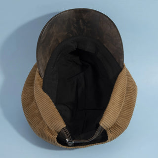 A vintage-style winter cap with a brown corduroy brim, a dark brown leather crown, and a black fabric lining, shown from a top-down view on a light blue background.