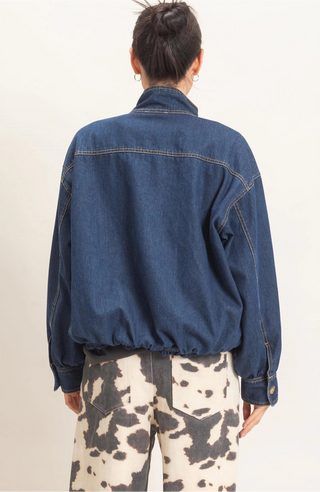 A person shown from the back wearing a dark blue denim jacket and cow-print pants against a plain off-white studio background.