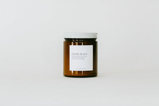 An amber glass jar candle with a white label reading 'INNER PEACE' and a white screw-top lid, centered on a clean white background.