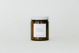 A single amber glass jar candle with a white lid and a white label reading 'HIGGGE' and 'The cozy, warm lighting you get from this candle is what makes this candle special.' on a clean white background.