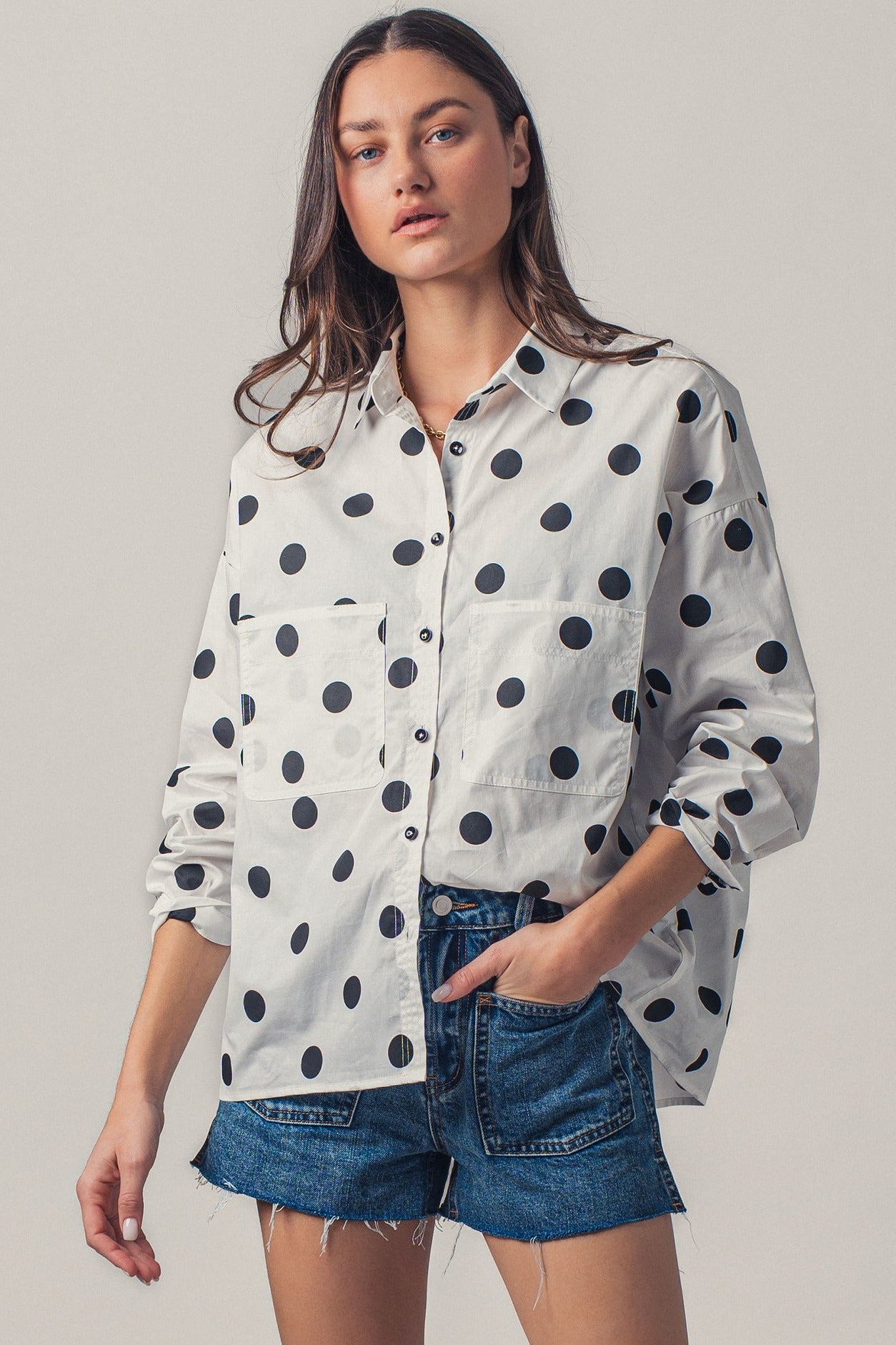 Woman wearing a white shirt with black polka dots and denim shorts on a plain background
