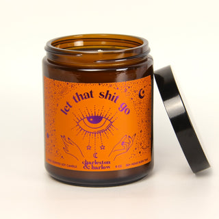 Candle jar with an orange label featuring text and symbols on a white background
