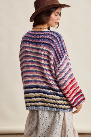 Woman wearing a colorful striped sweater and brown hat against a neutral background