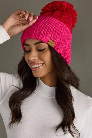 Woman wearing a bright pink knit beanie with a red pom-pom against a neutral background