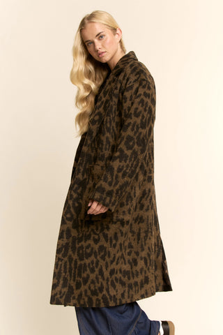 A woman modeling a mid-length brown and black leopard-print coat against a plain beige studio background.