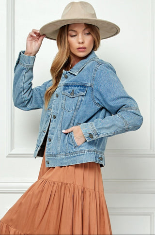 Woman wearing a denim jacket and beige hat against a white wall