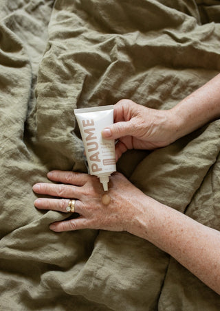 Hand applying cream from a 'PAUME' tube on a textured surface