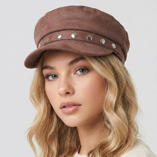 Woman wearing a brown cap with silver studs on a light gray background