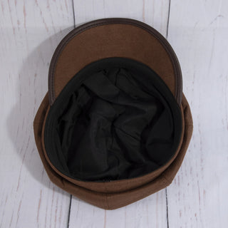 A brown flat cap with a black fabric lining, photographed from directly above on a white-painted wooden plank background.