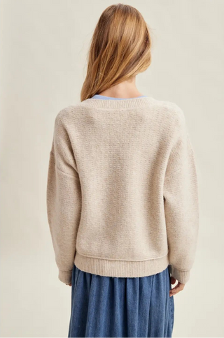 Person wearing a beige sweater and blue pants on a plain background