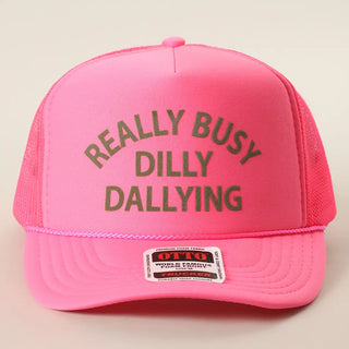 Pink trucker hat with 'REALLY BUSY DILLY DALLYING' text on a beige background