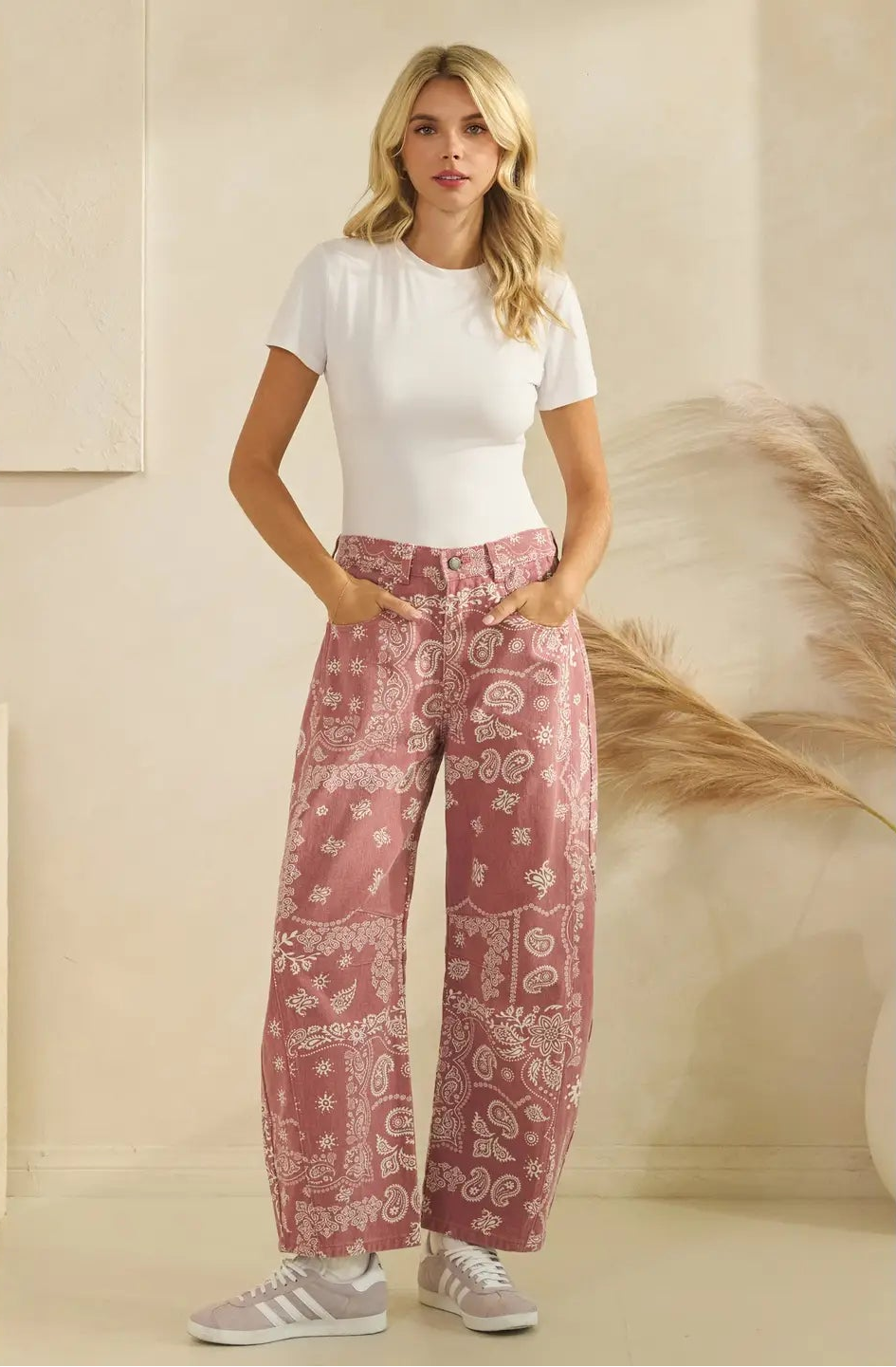 Woman wearing a white t-shirt and pink patterned pants against a neutral background