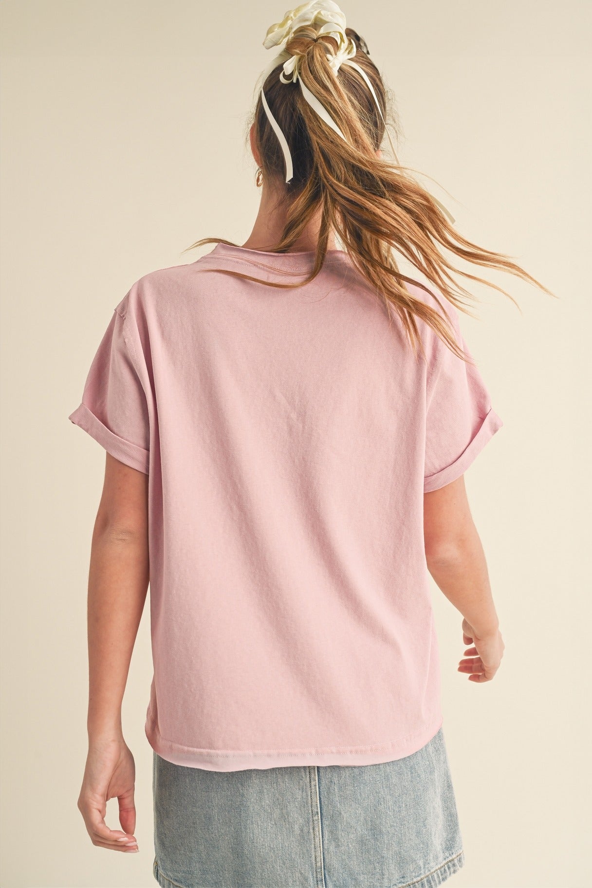 Person wearing a pink t-shirt and denim shorts on a beige background
