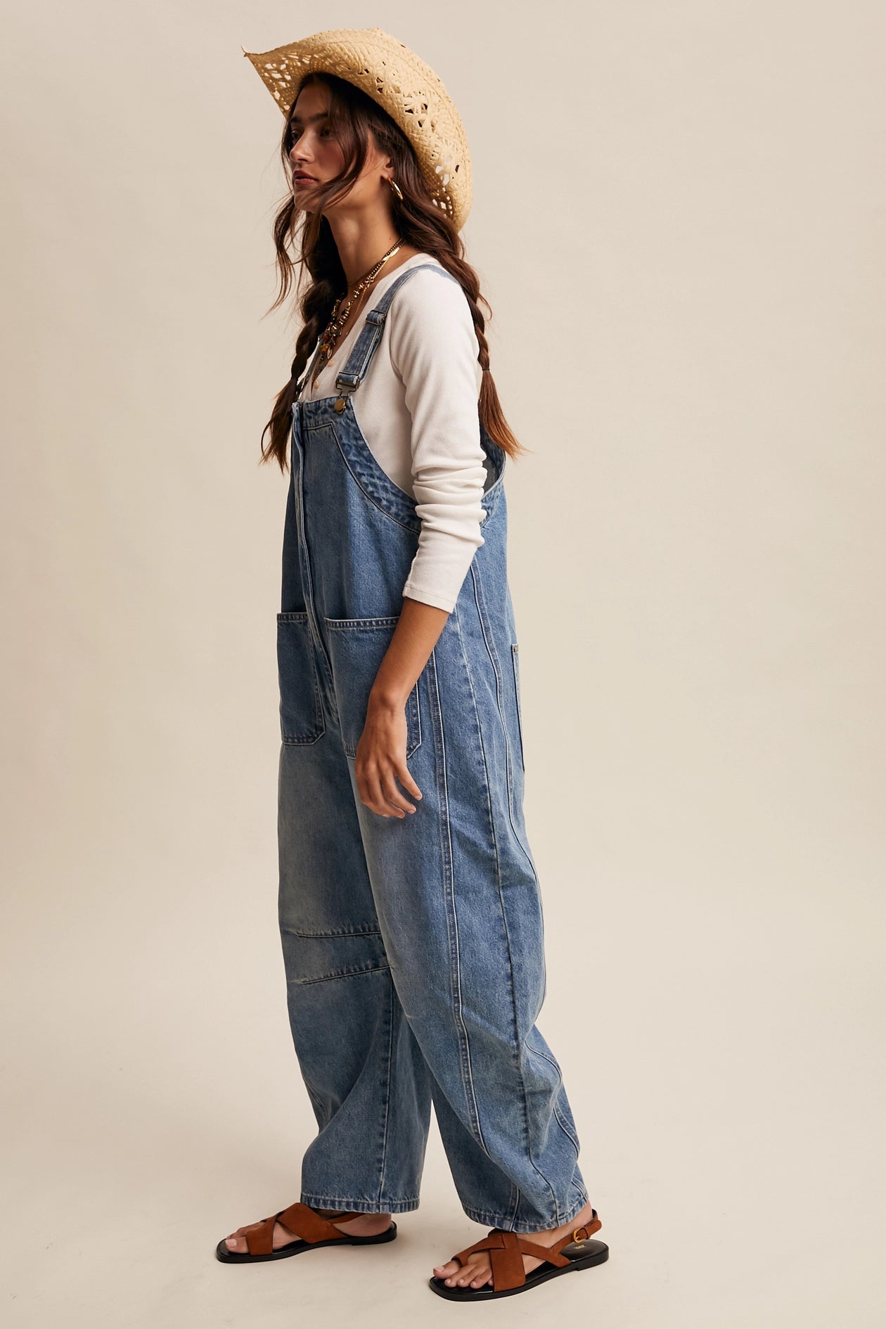 Woman wearing denim overalls and a straw hat on a beige background
