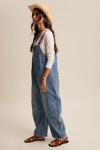 Woman wearing denim overalls and a straw hat on a beige background