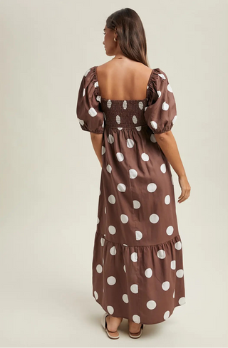 Women wearing brown polka dot dress against a neutral background. 