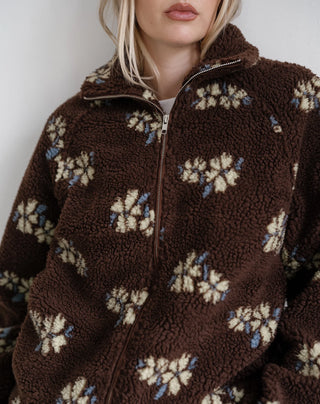 A close-up of a person wearing a brown sherpa fleece zip-up jacket with a cream and blue floral pattern, cropped from the mouth down against a plain light background.